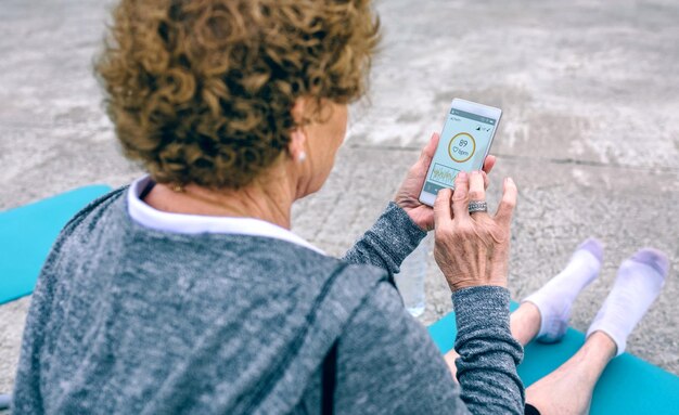 Vista traseira da mulher sênior irreconhecível usando smartphone pelo cais marítimo