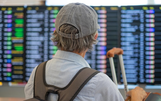 Vista traseira da mulher sênior no aeroporto olhando para o horário para verificar o portão de embarque do voo Pessoas do conceito de viajante com mochila e malas