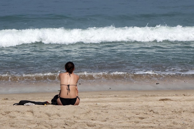 Vista traseira da mulher sexy em biquíni sentado na praia tropical de areia branca