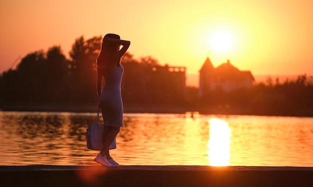Vista traseira da mulher solitária em pé no lado do lago na noite quente Conceito de solidão e relaxamento
