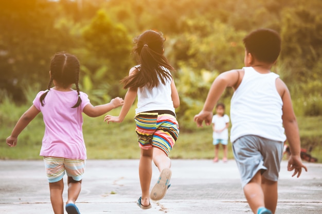 Vista traseira das crianças asiáticas se divertindo para correr e brincar juntos no campo