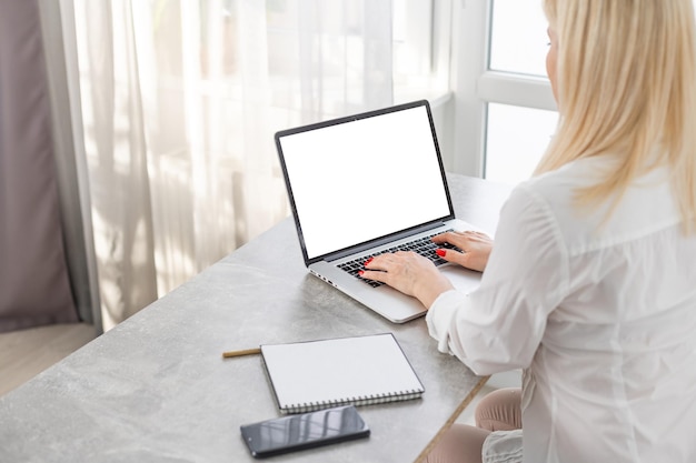 Vista traseira das mãos de mulher de negócios ocupadas usando laptop na mesa de escritório, com copyspace, contra a parede branca