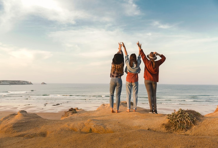 Foto vista traseira de amigas de pé na praia contra o céu durante o pôr do sol