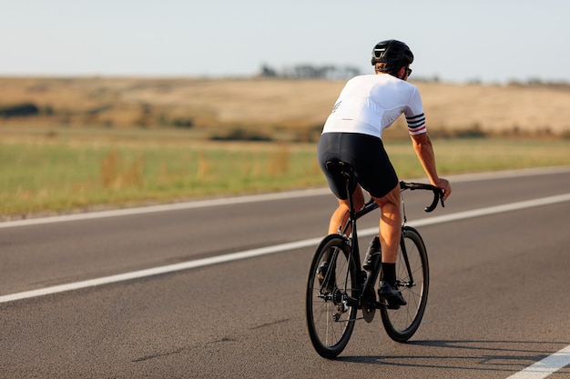 Vista traseira de ciclista profissional em roupas esportivas e capacete de bicicleta em estrada de asfalto