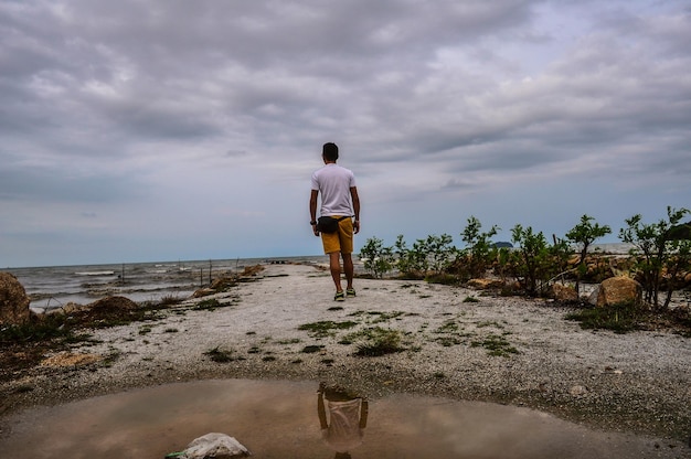 Foto vista traseira de comprimento completo de um homem de pé na praia contra o céu nublado