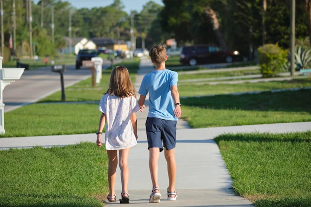 Vista traseira de dois jovens adolescentes menina e menino irmão e irmã caminhando juntos na rua rural no dia ensolarado brilhante conceito de tempo de férias