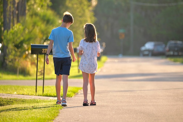 Vista traseira de dois jovens adolescentes menina e menino irmão e irmã caminhando juntos na rua suburbana na noite ensolarada