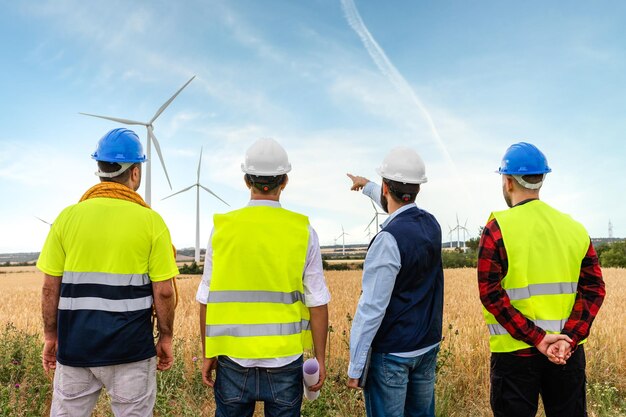 Foto vista traseira de engenheiros elétricos e trabalhadores de manutenção olhando para parques de turbinas eólicas