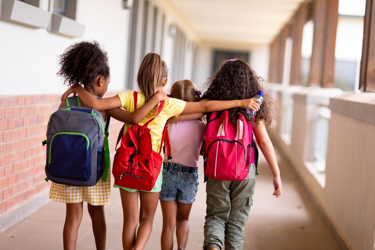 Foto vista traseira de estudantes multirraciais do ensino fundamental com mochilas e braços andando no corredor