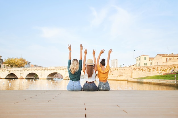 Foto vista traseira de felizes jovens mulheres amigas sentadas no lago