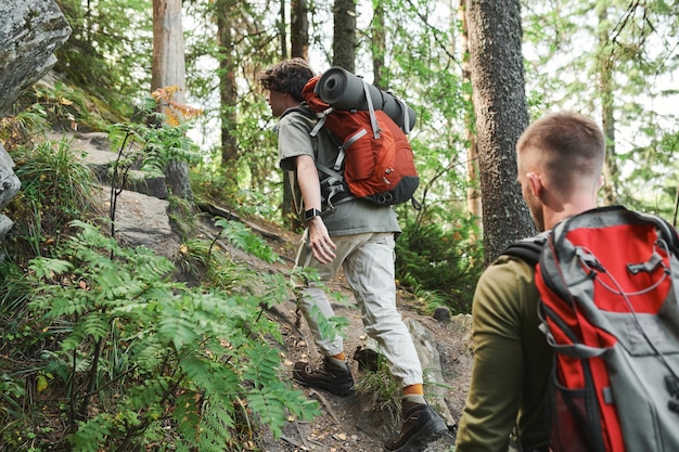 Vista traseira de jovens com mochilas escalando penhasco íngreme enquanto caminhava nas montanhas