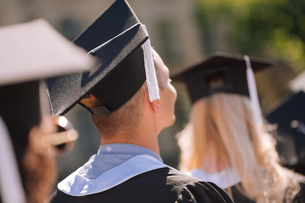 Vista traseira de jovens graduados usando capas de mestrado