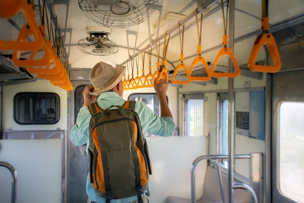 Vista traseira de mochileiros asiáticos segurando o corrimão dentro do trem público de férias