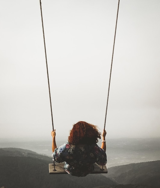 Foto vista traseira de mulher balançando em uma corda balançando contra o céu