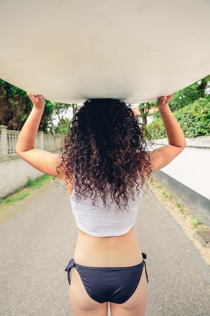 Foto vista traseira de mulher carregando prancha de surf na estrada