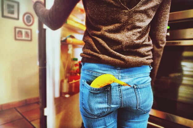 Foto vista traseira de mulher com banana no bolso abrindo a porta da geladeira