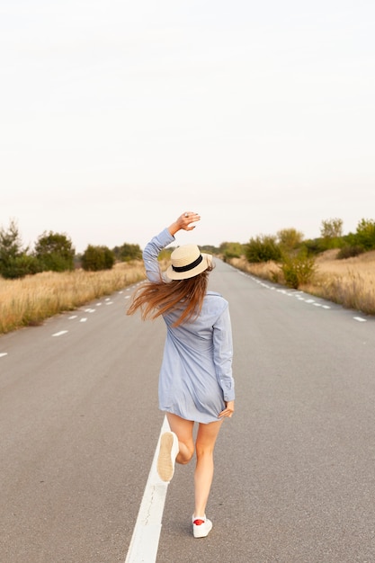 Foto vista traseira de mulher com chapéu correndo no meio da estrada