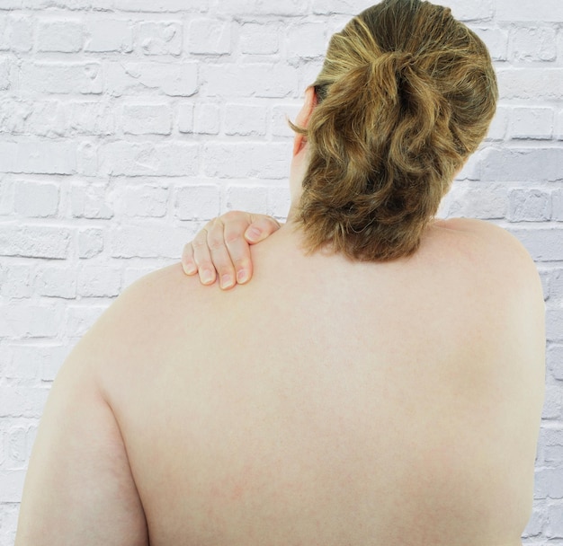 Foto vista traseira de mulher com excesso de peso com a mão no ombro de pé contra a parede branca