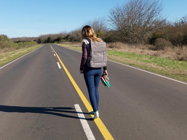 Foto vista traseira de mulher com mochila andando na estrada