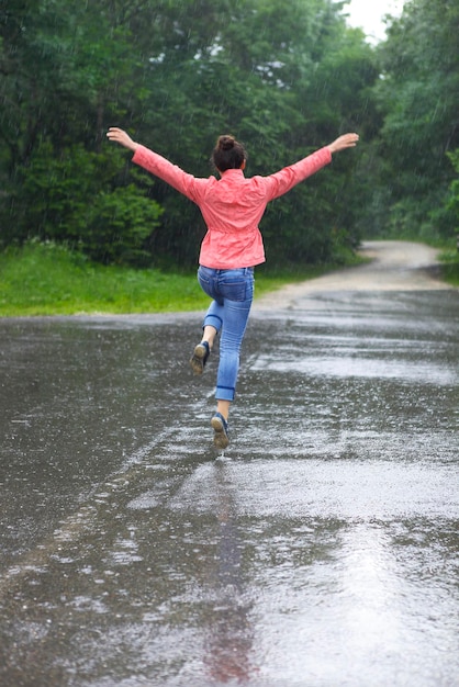 Foto vista traseira de mulher com os braços estendidos pulando na estrada durante a chuva