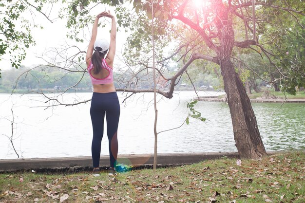 Vista traseira de mulher com os braços levantados de pé contra o lago