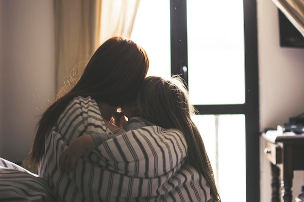 Vista traseira de mulher e filha cobertas de cobertor em casa