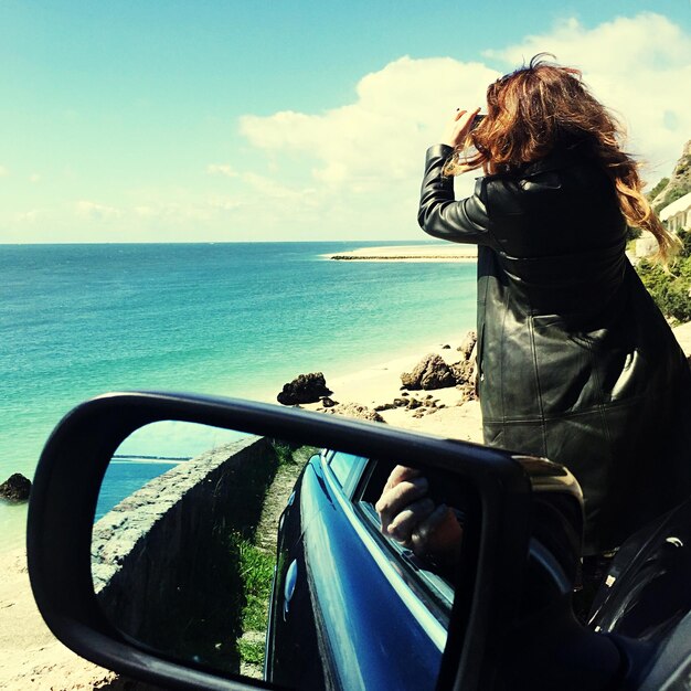 Foto vista traseira de mulher em carro fotografando o mar