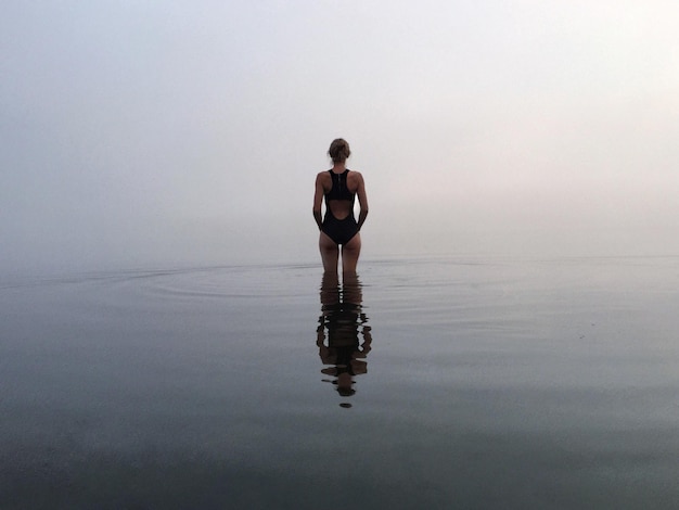 Vista traseira de mulher em trajes de banho no meio do mar durante o tempo nebuloso