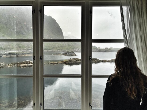 Foto vista traseira de mulher olhando para o rio e a montanha através da janela