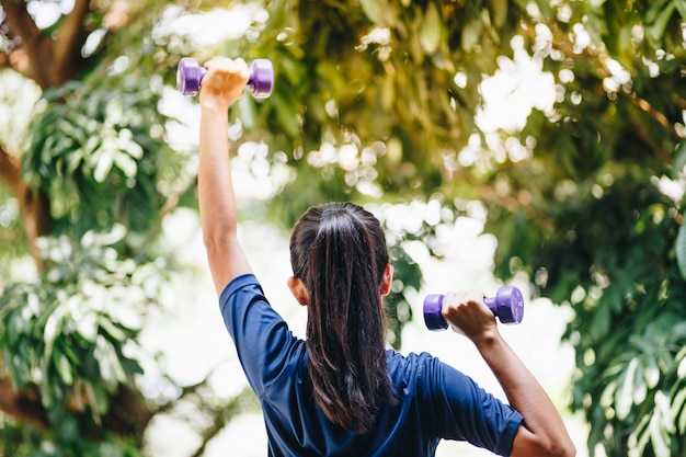 Foto vista traseira de mulher segurando halteres enquanto se exercita ao ar livre