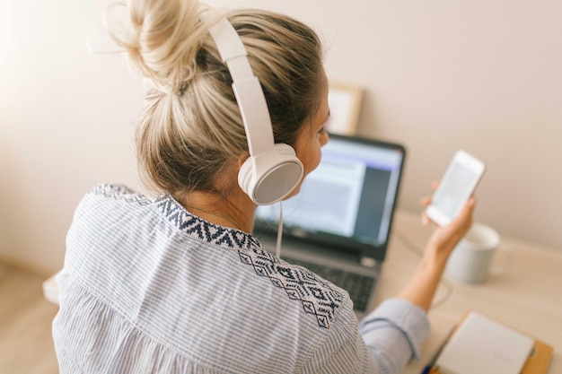 Vista traseira de mulher usando fone de ouvido segurando smartphone no escritório