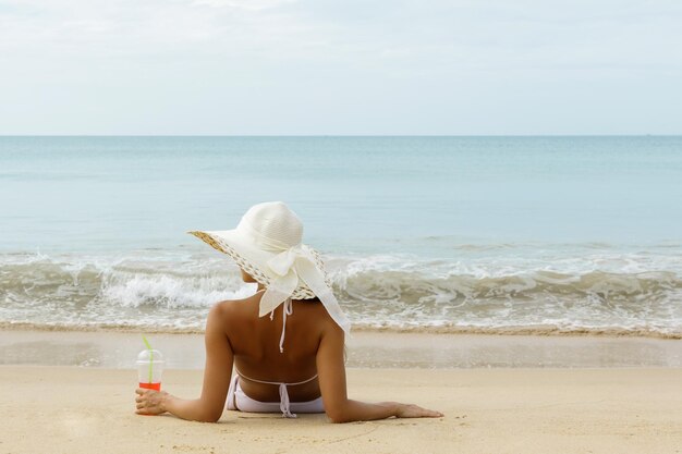 Foto vista traseira de mulher vestindo chapéu de pé na praia contra o céu