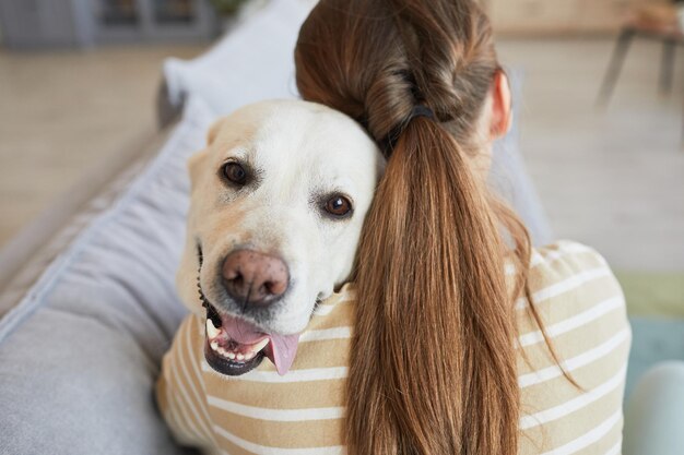 Vista traseira de perto de uma jovem acariciando um cachorro enquanto estava deitada no sofá em casa.