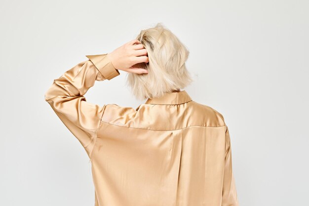 Vista traseira de pessoa com cabelo loiro em blusa de cetim mão na cabeça isolada em um fundo claro