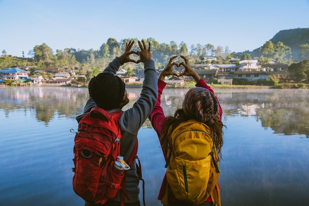 Foto vista traseira de pessoas fazendo forma de coração com as mãos enquanto estão de pé ao lado do lago contra o céu