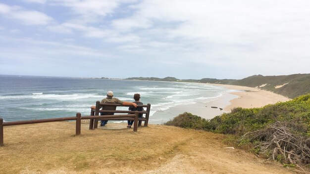 Foto vista traseira de pessoas sentadas na praia contra o céu