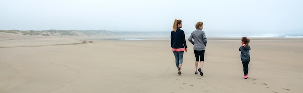 Vista traseira de três gerações femininas caminhando na praia no outono