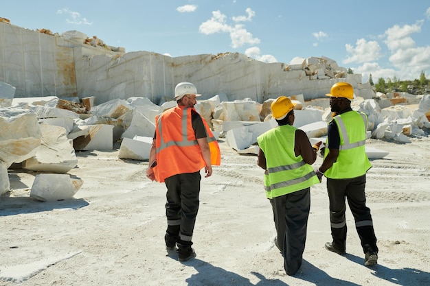 Vista traseira de três trabalhadores da pedreira de mármore movendo-se pelo território da fábrica