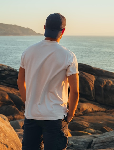 Vista traseira de um adolescente irreconhecível com as mãos nos bolsos olhando o mar.