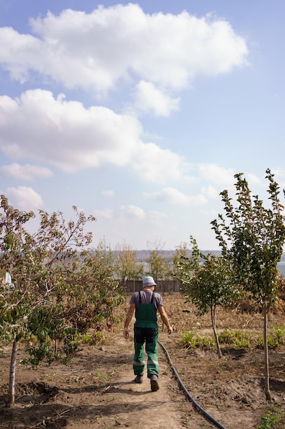 Vista traseira de um agricultor em movimento andando por seu jardim com árvores com céu e nuvens no horizonte