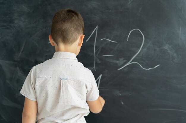 Vista traseira de um aluno em uma classe escreve números de giz em um quadro-negro lição de matemática conceito de educação da escola secundária de volta à escola lugar para texto