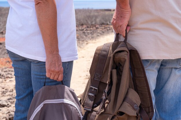 Vista traseira de um casal de viajantes idosos segurando suas mochilas, desfrutando de uma excursão ao ar livre. Horizonte sobre o mar e dia ensolarado