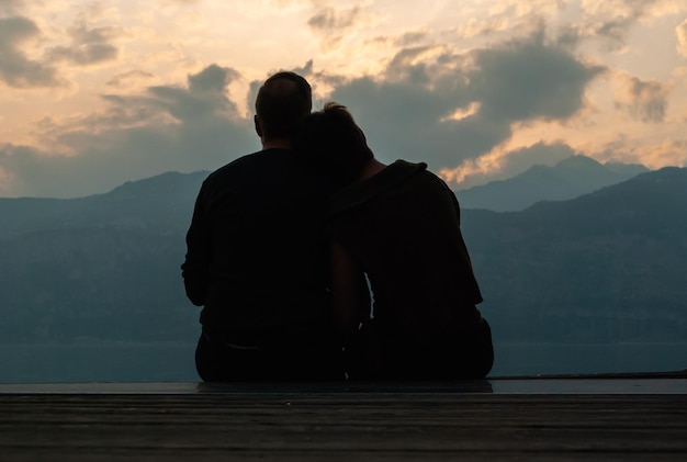 Vista traseira de um casal descansando enquanto olha para as montanhas durante o pôr-do-sol