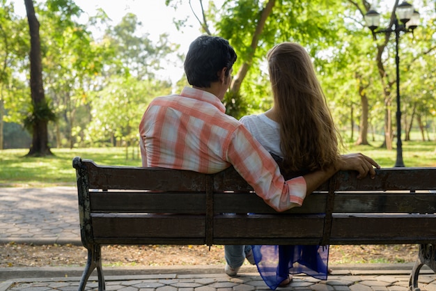 Vista traseira de um casal multiétnico sentado em um banco de madeira