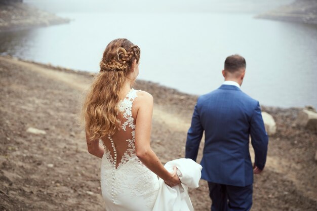 Vista traseira de um casal recém-casado caminhando em direção ao lago em um dia de nevoeiro