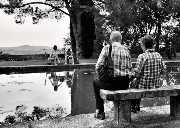 Foto vista traseira de um casal sentado à beira do lago