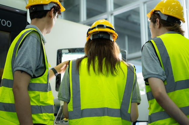 Foto vista traseira de um grupo de jovens trabalhadores de fábrica vestindo um capacete de segurança olhando para uma tela de computador