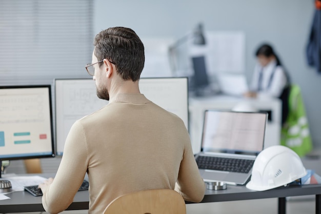 Vista traseira de um homem adulto barbudo trabalhando como engenheiro no local de trabalho com um chapéu em um espaço de cópia de mesa