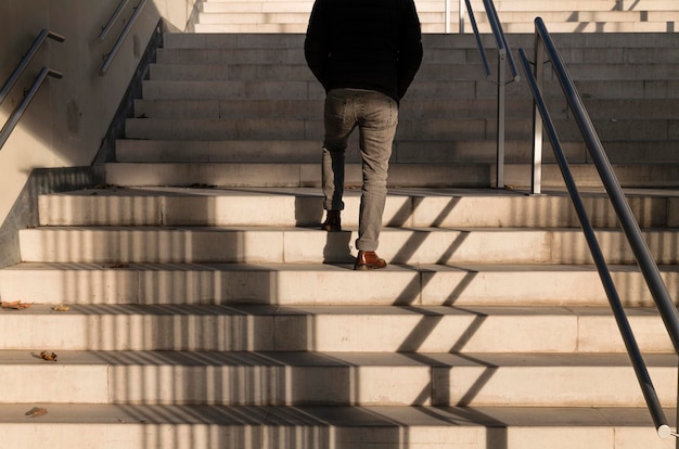 Foto vista traseira de um homem adulto caminhando pelas escadas com a luz do sol e a pessoa da sombra