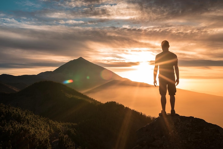 Foto vista traseira de um homem adulto de pé em uma rocha contra um céu nublado durante o pôr do sol